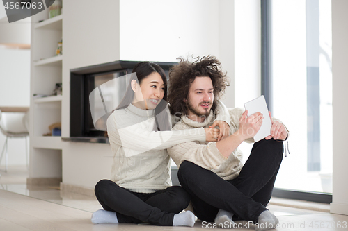 Image of multiethnic couple using tablet computer in front of fireplace