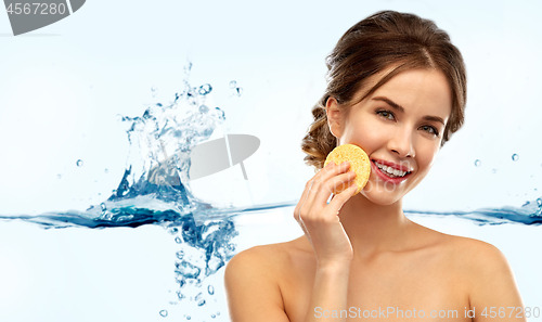 Image of young woman cleaning face with exfoliating sponge