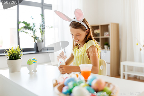 Image of happy girl coloring easter eggs at home