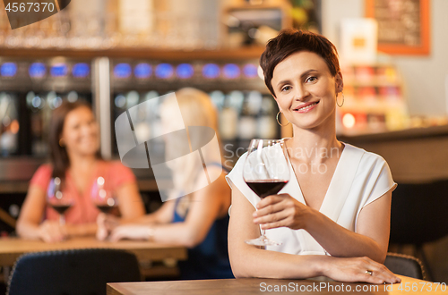 Image of happy woman drinking red wine at bar or restaurant