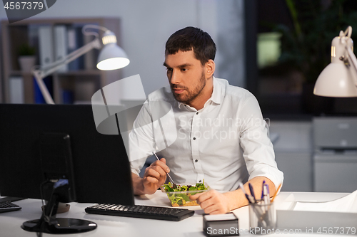 Image of businessman with computer eating at night office