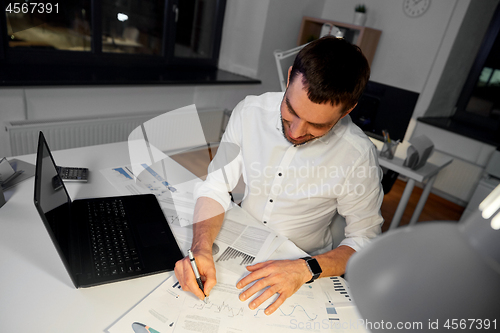 Image of businessman with papers and laptop at night office