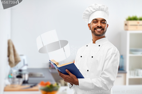 Image of happy male indian chef with cookbook at kitchen