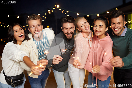 Image of happy friends with sparklers at rooftop party