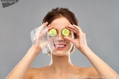Image of smiling woman with cucumber over grey background