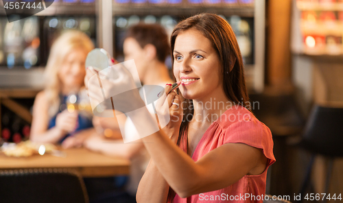 Image of woman with lipstick applying make up at restaurant