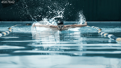 Image of dynamic and fit swimmer in cap breathing performing the butterfly stroke