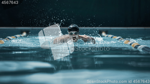 Image of dynamic and fit swimmer in cap breathing performing the butterfly stroke