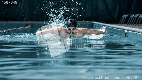 Image of dynamic and fit swimmer in cap breathing performing the butterfly stroke