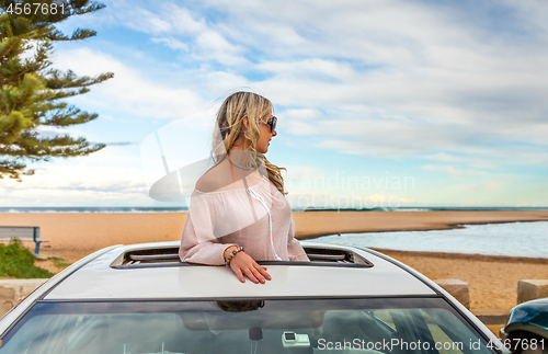 Image of Road trip summer beach vibes.  Carefree woman in sunroof car by 