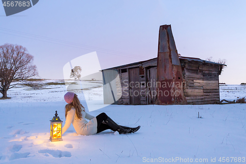 Image of Woman with lantern sitting in a snow covered field