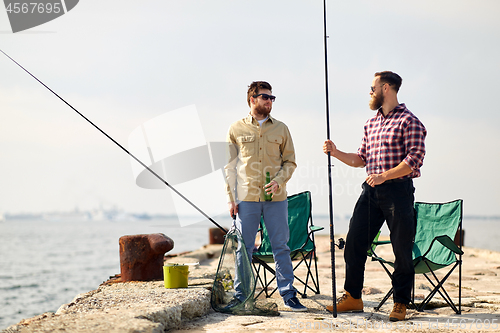 Image of happy friends with fishing rods and beer on pier