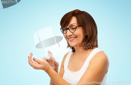 Image of smiling senior woman spraying perfume to her wrist