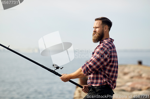 Image of bearded fisherman with fishing rod on pier at sea