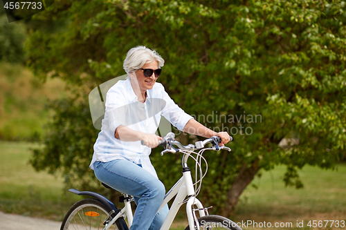 Image of happy senior woman riding bicycle at summer park