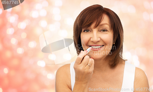 Image of smiling senior woman applying lipstick to her lips