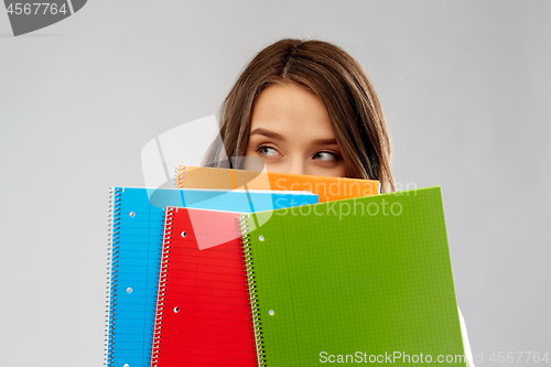 Image of teenage student girl hiding behind notebooks