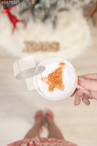 Image of Female holding cappuccino with Christmas tree design on froth