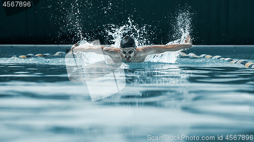 Image of dynamic and fit swimmer in cap breathing performing the butterfly stroke