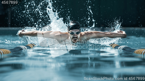 Image of dynamic and fit swimmer in cap breathing performing the butterfly stroke