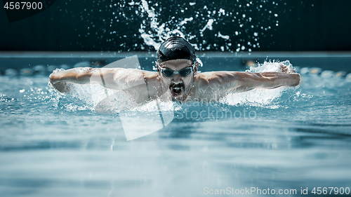 Image of dynamic and fit swimmer in cap breathing performing the butterfly stroke