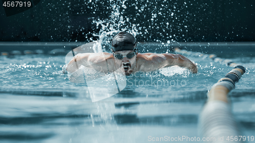 Image of dynamic and fit swimmer in cap breathing performing the butterfly stroke