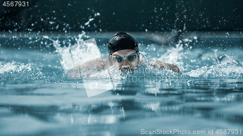 Image of dynamic and fit swimmer in cap breathing performing the butterfly stroke