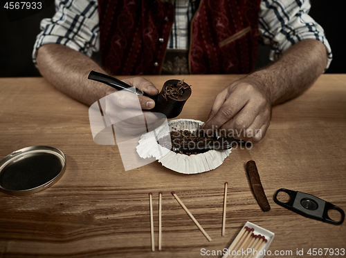 Image of bearded man clogs the tobacco in pipe