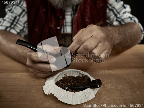 Image of bearded man clogs the tobacco in pipe