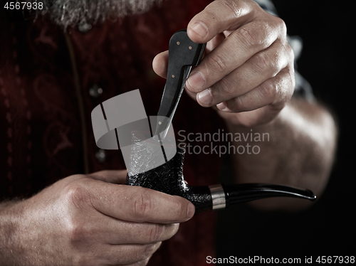 Image of bearded man clogs the tobacco in pipe