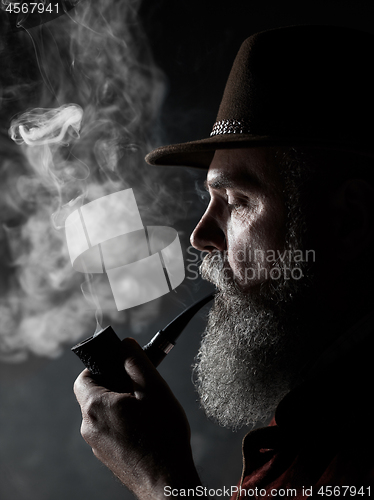 Image of Black and white dramatic portrait of senior smoking tobacco pipe