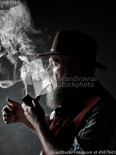 Image of Black and white dramatic portrait of senior smoking tobacco pipe