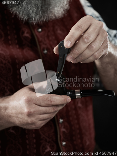 Image of bearded man clogs the tobacco in pipe