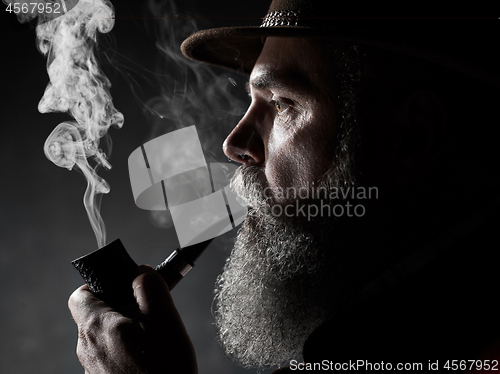 Image of Black and white dramatic portrait of senior smoking tobacco pipe