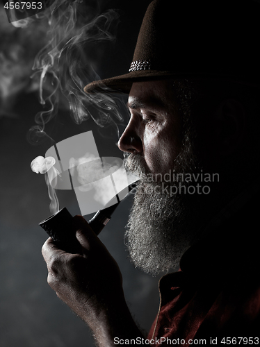 Image of Black and white dramatic portrait of senior smoking tobacco pipe