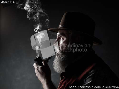 Image of Black and white dramatic portrait of senior smoking tobacco pipe