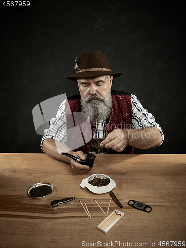 Image of bearded man clogs the tobacco in pipe