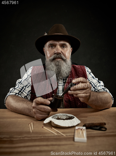 Image of bearded man clogs the tobacco in pipe