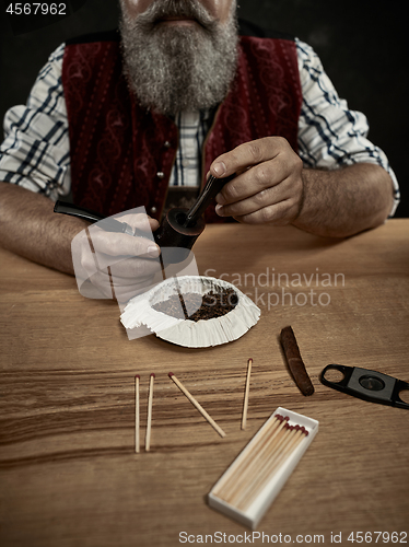 Image of bearded man clogs the tobacco in pipe