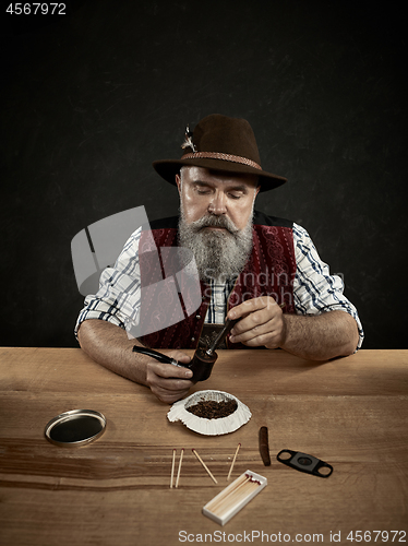 Image of bearded man clogs the tobacco in pipe