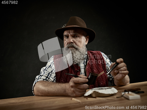 Image of bearded man clogs the tobacco in pipe
