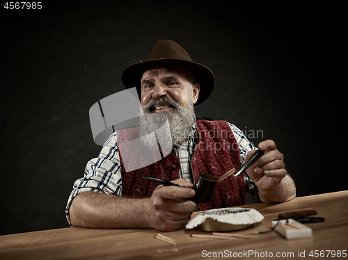 Image of bearded man clogs the tobacco in pipe