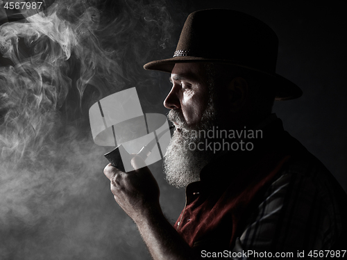 Image of Black and white dramatic portrait of senior smoking tobacco pipe