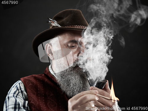 Image of Black and white dramatic portrait of senior smoking tobacco pipe