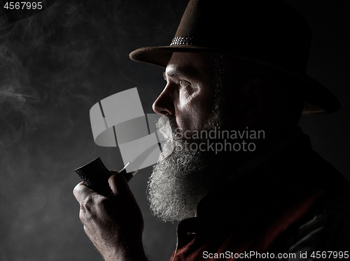 Image of Black and white dramatic portrait of senior smoking tobacco pipe