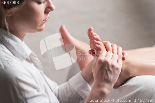 Image of Professional female masseur giving reflexology massage to woman foot