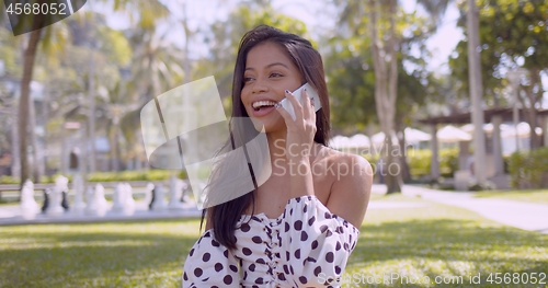 Image of Lively Asian woman in dress with open shoulder talking on smartphone