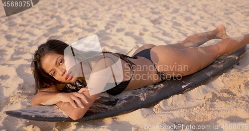 Image of Woman lying on surfboard and sunbathing on beach