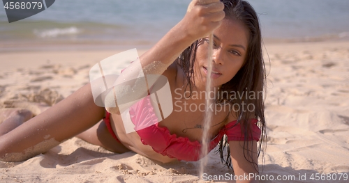 Image of Hot tanned woman with sand flowing through hand relaxing on beach