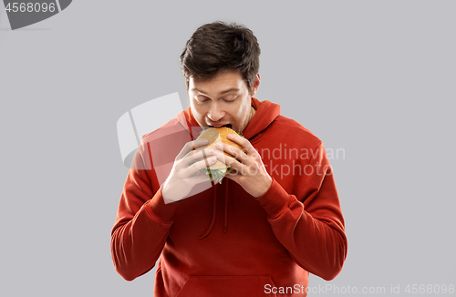 Image of hungry young man eating hamburger